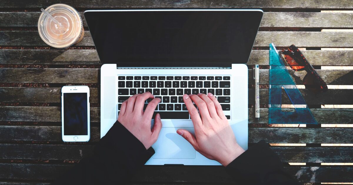 屋外のテーブルでノートパソコンを操作する手元