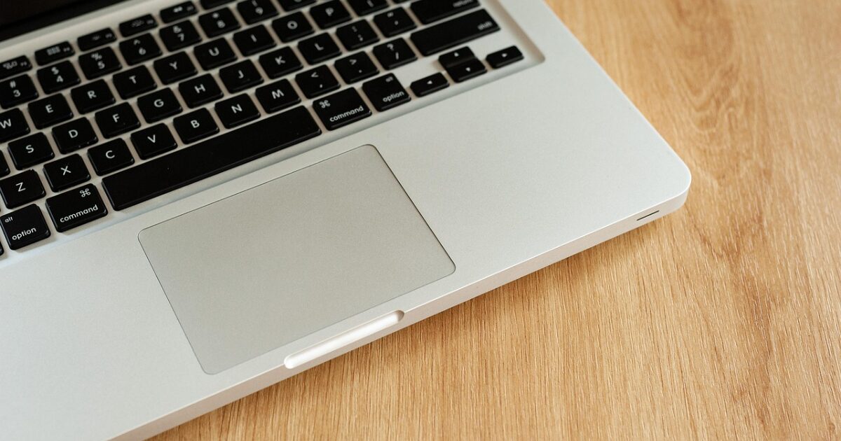 木製デスクに置かれたシルバーノートパソコンのトラックパッド部分