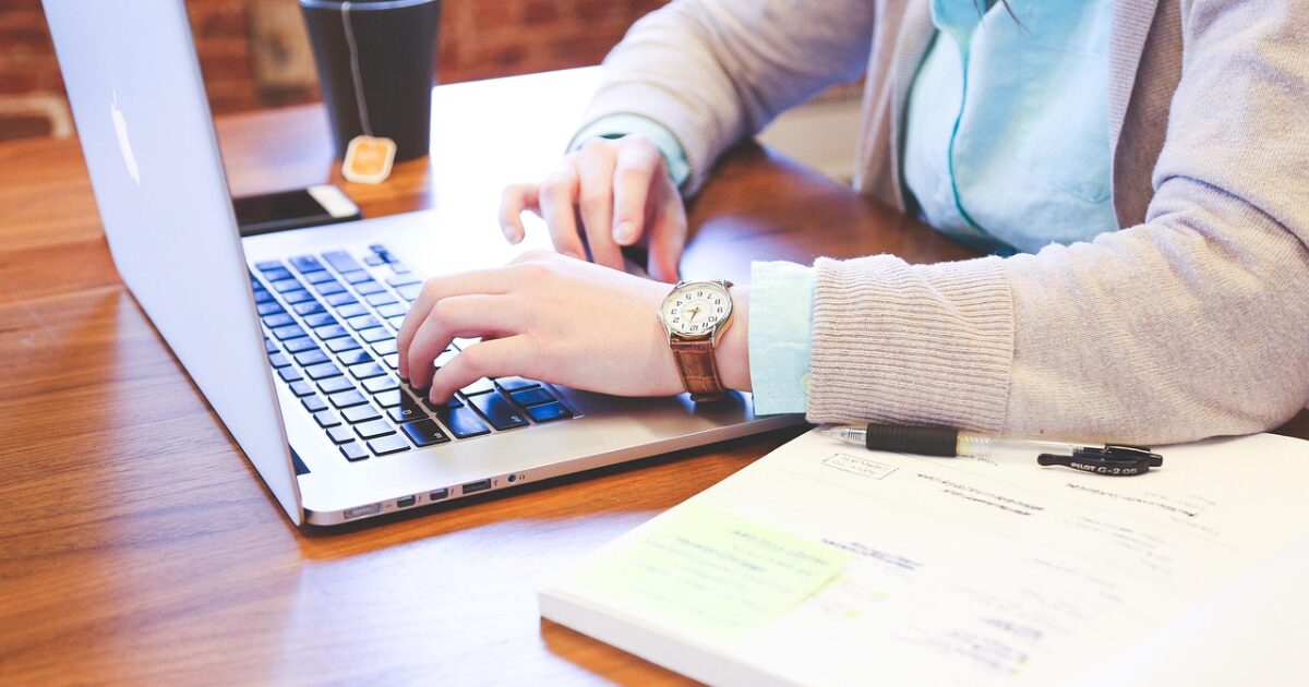 木製テーブルでノートパソコンを操作する人物と資料