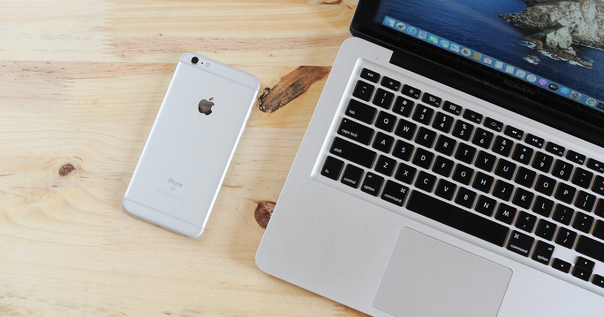 木目のデスク上に置かれたMacBookとiPhoneのミニマルな配置