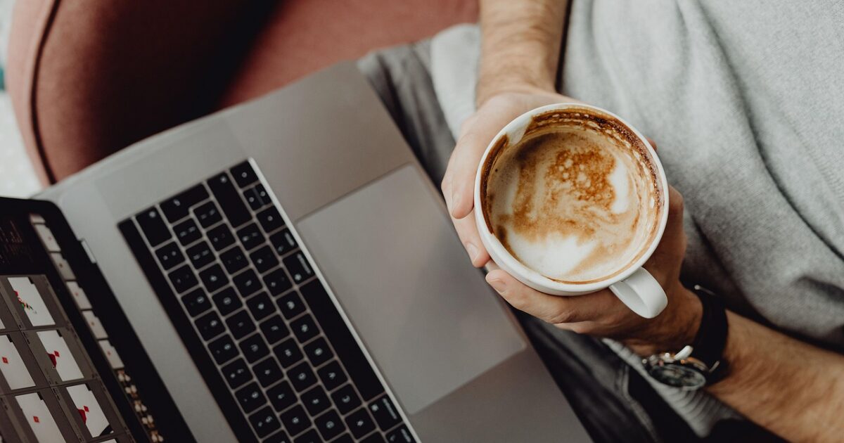 ノートパソコンを使いながらカフェラテを手に持つリラックスした作業風景