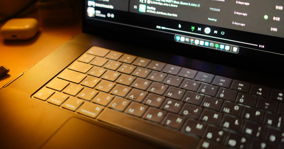 暗がりの中で音楽アプリが表示されたノートパソコンのバックライト付きキーボード