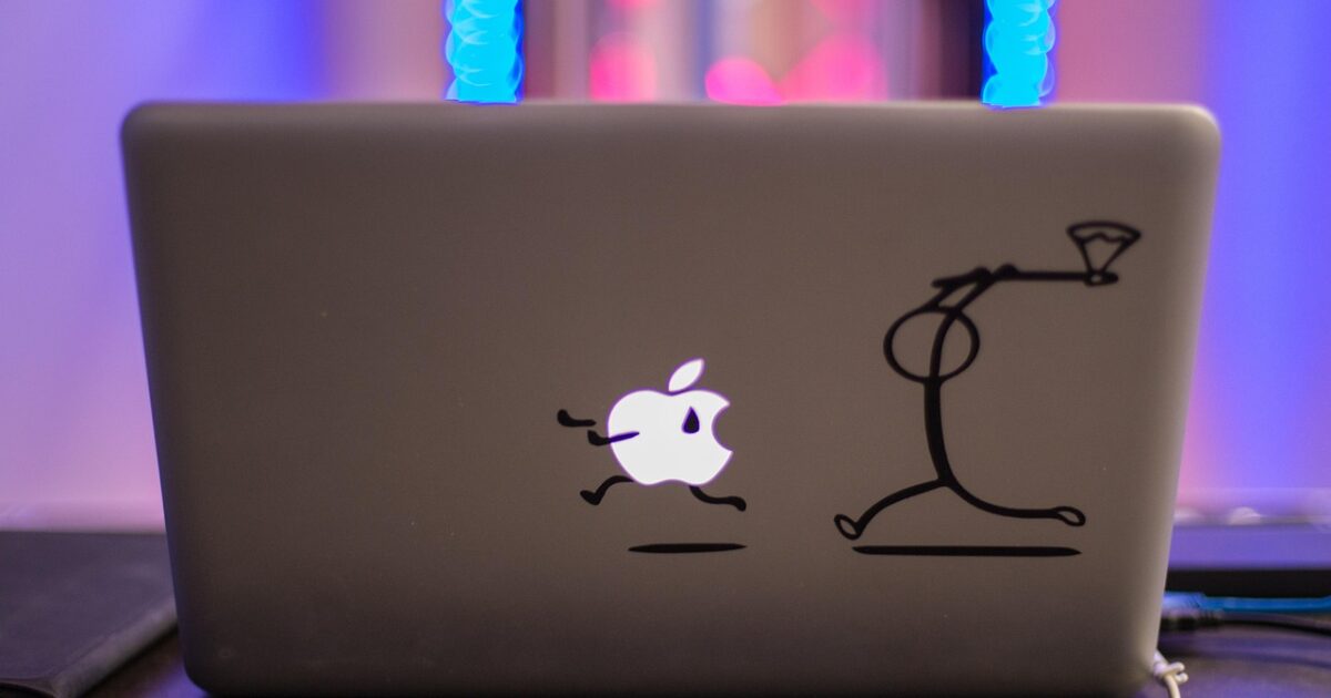 Appleロゴにユニークなステッカーが貼られた黒いノートパソコンの背面